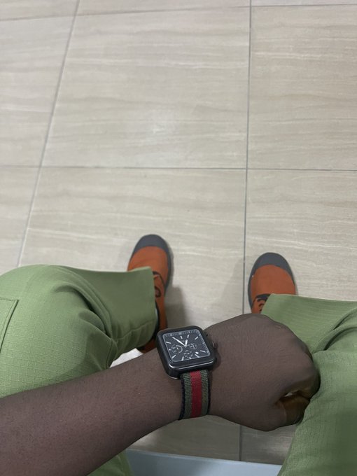 A person wears an Apple Watch with a red and green striped band, paired with orange shoes and green pants, standing on a tiled floor—symbolizing "arc-hitect" style and a stylish, ready-to-build vibe for the agentic economy on Arc.