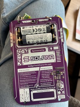 A purple Solara device badge or card containing two AA batteries, sponsored by Solara with text indicating it is 'Made with ♡ by Hack the North', hanging against someone's blue jeans.