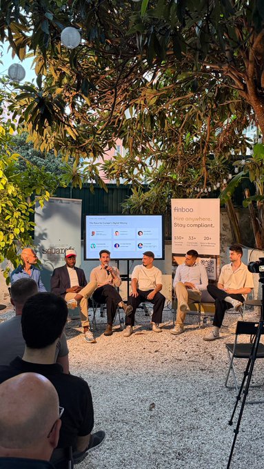Outdoor panel discussion with five men seated on chairs in front of screens displaying 'The Rule Of 5 Web3 Talent,' under trees with white paper lanterns, with 'finboo. Hire anywhere. Stay compliant.' banner visible.