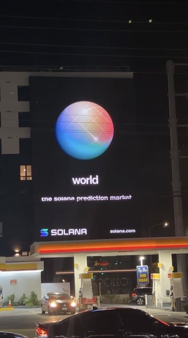 An illuminated nighttime billboard advertises Solana as 'the solana prediction market' with 'world' displayed prominently beneath a colorful sphere logo.