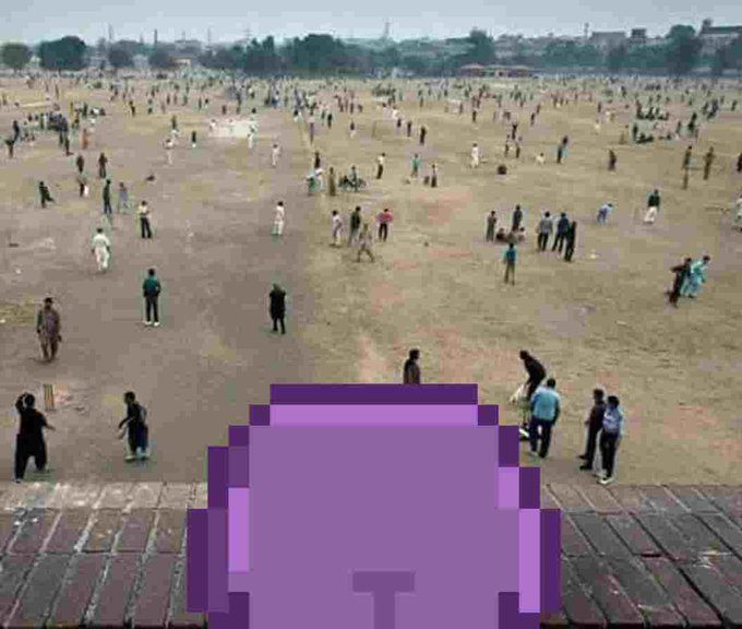 An aerial view of a large, sparsely populated grassy field with many small figures of people scattered across it, with a purple pixelated 'T' logo overlay in the foreground.