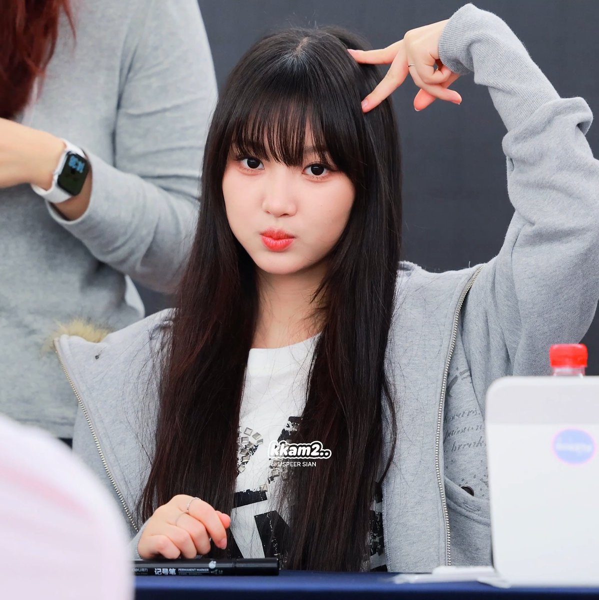 A young woman with long black hair poses with a peace gesture near her head at what appears to be a fan event, with 'Sakam2' and 'Jispeersian' watermarks visible.