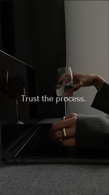 A moody image of hands on a laptop keyboard while holding a wine glass, overlaid with the motivational text 'Trust the process.'