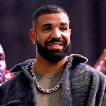 A smiling man with a beard wearing a gray hoodie and an iced-out Cuban link chain necklace.