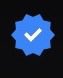 A blue scalloped badge with a white checkmark in the center, resembling the familiar Twitter/X verification badge, displayed against a black background. The image visually references the "blue check" mentioned in the post, humorously tying it to the OpenSea NFT platform.