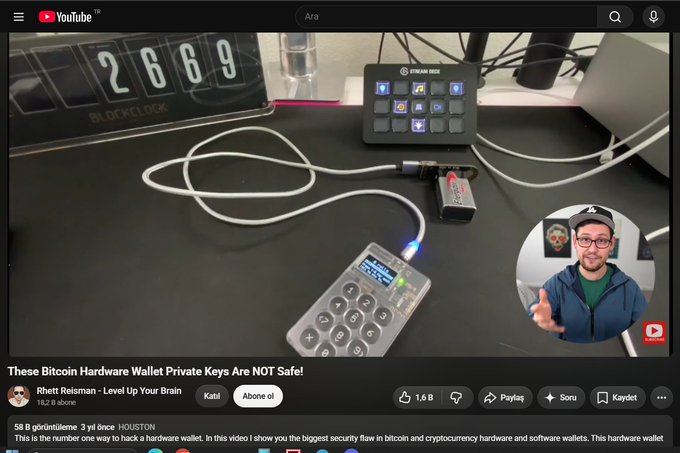 The image shows a YouTube video titled "These Bitcoin Hardware Wallet Private Keys are NOT Safe!" by Rhett Reisman, featuring a man in a blue cap and hoodie alongside a desk setup displaying a BlockClock showing "2669," a Stream Deck, a Coldcard hardware wallet, and a USB adapter. This relates to the post by highlighting the video's demonstration of a hardware wallet vulnerability that allegedly led to the theft of over 1000 $btc, with the attack logic mirroring the scenario shown.