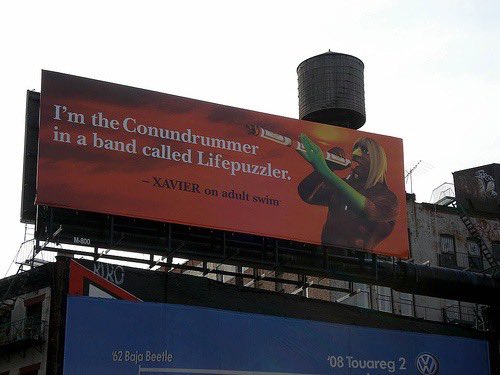 An outdoor billboard advertisement featuring a cartoon character playing a trumpet, with the text: 'I'm the Conundrumrummr in a band called Lifepuzzler. - XAVIER on adult swim.'