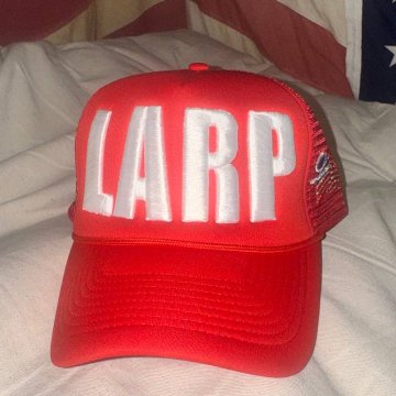 A bright red mesh trucker hat sits on a white fabric surface, featuring the large white letters "LARP" on the front panel.