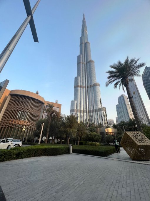 A view of the Burj Khalifa skyscraper towering over palm trees in Dubai, next to a modern building.
