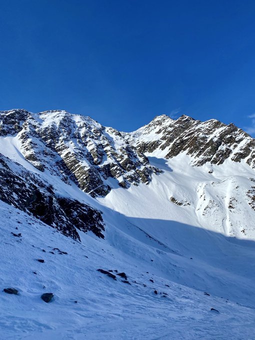 Snow-covered mountain peaks under a clear blue sky with rocky outcrops scattered across the slopes.
