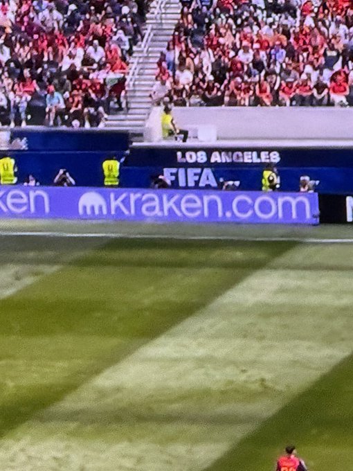 A crowd fills the stands at a soccer stadium with "LOS ANGELES" and "FIFA" signage visible alongside a "kraken.com" advertisement banner, connecting the post's tag of @krakenfx. A player in a pink jersey stands on the field in the foreground. The mention of $ELON #DogelonMars appears to play on the Los Angeles venue and Elon Musk's local ties.