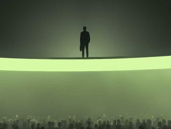 A silhouetted person holding a bag stands on a brightly illuminated circular stage above a dim audience.