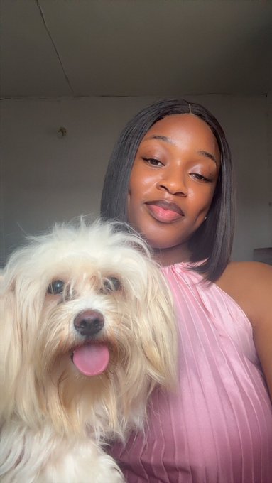 A woman in a pink halter top poses for a selfie with her fluffy cream-colored dog, both looking happy and relaxed in a casual indoor setting. The cozy, cheerful vibe of the image complements the upbeat Sunday morning greeting and positive energy toward $RIVER/@River4fun shared in the post.