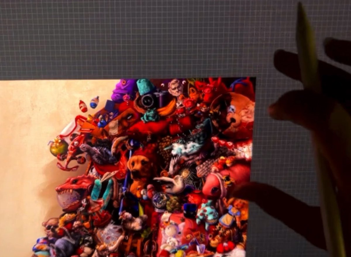 A colorful collage image featuring many small toys, animals, and objects arranged into a larger shape is held against a blue grid cutting mat.