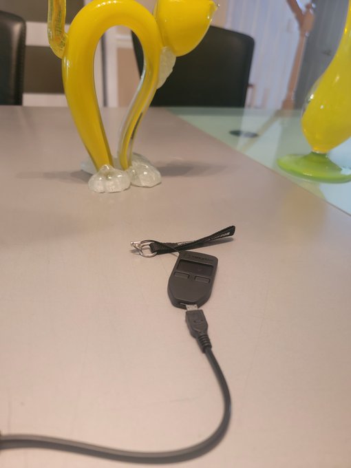 A black Trezor hardware wallet with two buttons and an attached USB cable sits on a white table near a yellow glass figurine, reflecting the post's mention of barely getting the Trezor connected and safeguarding crypto funds.