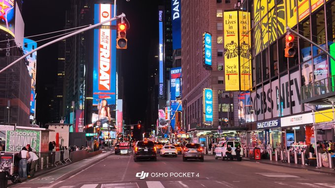 A nighttime view of Times Square in New York City with bright billboards, taxi cabs, and pedestrians, watermarked with 'DJI OSMO POCKET 4'.