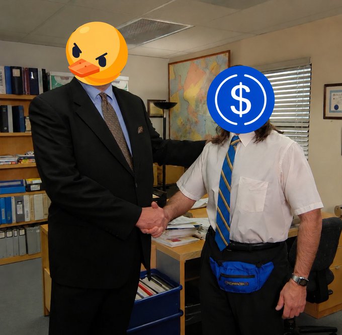 A humorous photoshopped image of two men shaking hands in an office, with one face replaced by an angry duck emoji and the other by the blue USDC cryptocurrency logo.