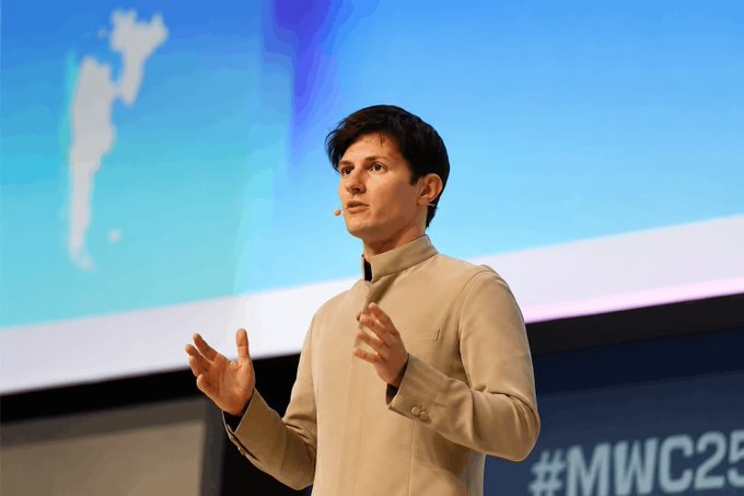 A man with dark hair, wearing a beige jacket and a headset microphone, speaks on stage with expressive hand gestures, with "#MWC25" visible in the bottom right corner of the display behind him. The image illustrates Pavel Durov's announcement at Mobile World Congress 2025 about Telegram's upcoming non-custodial crypto wallet rollout to its massive user base.
