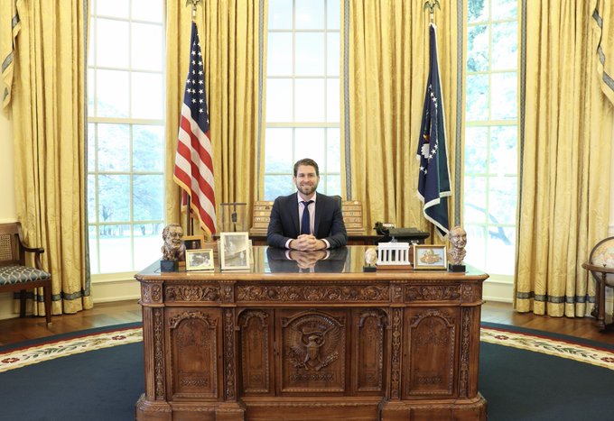 The image shows a man in a suit smiling while seated at the Resolute Desk in the Oval Office, with the American flag and presidential flag displayed behind him. The accompanying post references "@MLeeJr" as a trusted figure associated with @base, with the Oval Office setting likely being a humorous comparison suggesting leadership or authority.

Note: The caption is generic because no identifying text, names, or ticker symbols are visible in the image itself to confirm the individual's identity.