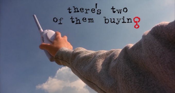 A person holds a baby monitor against a cloudy background, overlaid with the text 'there's two of them buyin' accompanied by a red figure-eight symbol.