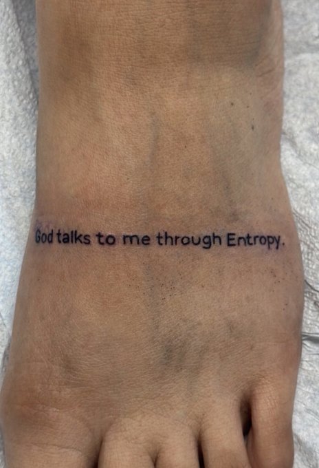 A person's foot has the tattoo "God speaks to me through Entropy." across the top of it, personally embracing the concept referenced by the $ENTROPY ticker.