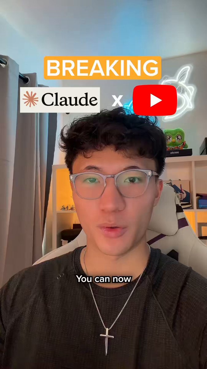The image features a man wearing glasses with a cross necklace and appears to be speaking into a video camera during a break-up event, possibly via YouTube. He has dark hair and is dressed for colder weather with an overcoat on his shoulders. The background reveals a room with a window and curtains providing some privacy. There are several other people in the image who might be present at the break-up event or merely observing. Additionally, there is text near the bottom of the image that reads "BREAKING CLAude x CLUDE." It seems that there's an association between the man speaking into the video camera and a particular brand, potentially CluDe, as indicated by the caption. The context and setting suggest that this could be part of a promotional campaign for someone related to the brand or a similar event taking place on YouTube.