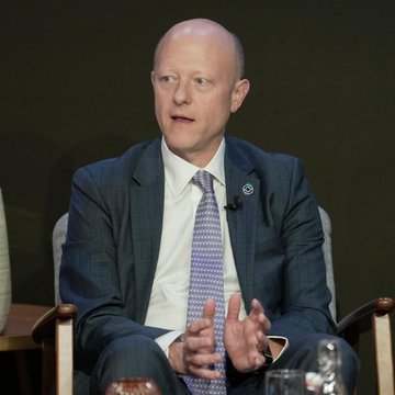 A man, appearing to be Jeremy Allaire, sits in a chair wearing a dark suit, white shirt, and patterned tie, gesturing with his hands as if speaking at a panel or event. The image relates to the accompanying post as it likely depicts Jeremy Allaire, the Circle CEO mentioned in the statement about agent-to-agent transactions being settled in USDC.