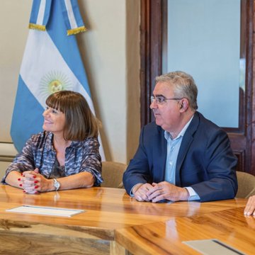 Two officials sit at a wooden conference table during the launch of "Catamarca On-Chain," a digital governance and blockchain initiative, with the Argentine flag displayed behind them and the partial number "100" visible on documents in the foreground.
