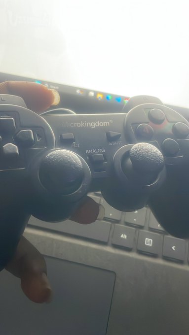 A close-up photo of a person holding a black Microkingdom wireless game controller in front of a laptop, with a finger resting on the touchpad.