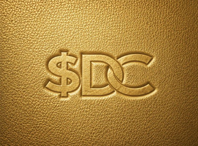 The image features a gold-colored leather surface with the words "SDC" written in an elegant cursive font, which appears to be a logo or tagline for a project called Solana. The text "DC under @benxchain is a Solana token with a fixed 1B supply which is built more as an ecosystem entry point than a standalone asset." This suggests that the image might be related to a project or initiative named "SDC" and that it involves the use of Solana tokens, which are digital assets tied into a specific ecosystem. The text also mentions staking, governance, NFTs for tiered access, and a launchpad for incoming projects, indicating that this project is likely focused on blockchain technology and tokenization.
