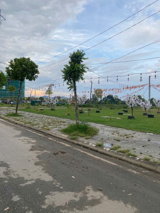 The image depicts a quiet roadside scene with a tree, string lights, and bunting flags in an empty park area, which visually echoes the post's warning about deceptive KOLs—fancy setups that create hype and FOMO but mask the emptiness and lack of substance behind their promises of guaranteed returns.