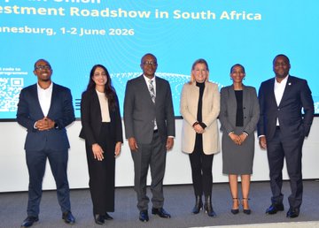 The image features a group of six people standing next to each other, all dressed professionally for an event or presentation. They are posing together for a photo, with some individuals wearing ties as part of their attire. The backdrop behind them displays information about an event related to investment in Africa and the World Investment Forum.
