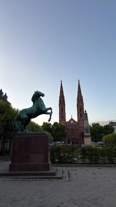 A striking bronze horse statue stands before the impressive red brick Marktkirche in Wiesbaden, a fitting centerpiece for the city's beauty.