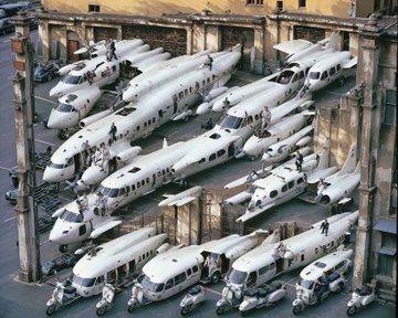 An aerial view of numerous private jets and helicopters tightly packed into an enclosed courtyard or hangar space.
