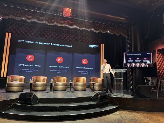 A man gives a presentation on a stage with gold chairs, in front of a screen displaying 'NFT builder, AI engineer, Infrastructure lead' with sections for NFT Product & Tooling, AI-Native Development, and Protocol Infrastructure.