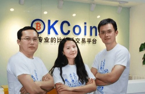 The image features three people standing together in front of a glass wall with the words "OK Coin" written above them, indicating that they are part of an OK Coin team or company. The individuals appear to be posing for a photo, possibly at their workplace or during a meeting.