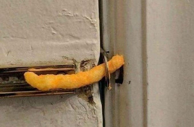 A corn dog or fried food item wedged between a door and its frame, held in place by the door latch.