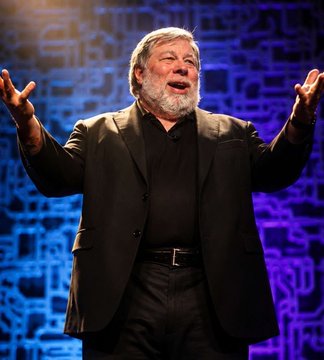 Apple co-founder Steve Wozniak is shown speaking on stage with his arms raised, appearing enthusiastic—aligning with his quote praising Bitcoin as "better than gold."