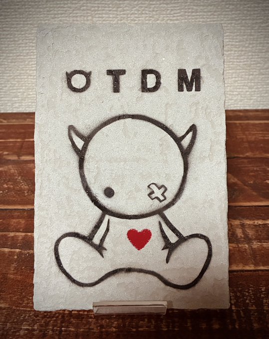 A handmade card featuring a drawing of a small horned monster character with one X-shaped eye and a red heart on its chest, with the text 'OTDM' written at the top.