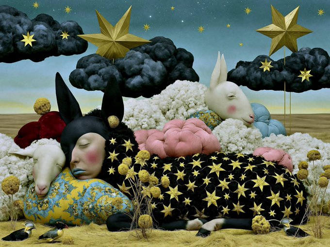 Whimsical surrealist artwork featuring anthropomorphic animal figures (a sheep, a donkey, and a rabbit) lying on a star-patterned bed amid a dreamlike landscape with dark clouds and golden stars.