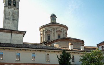 The image features an old, large building with a dome and a clock tower. The building has a clock located at the top of its structure. In front of the building, there are two trees that add some greenery to the scene. The sky above is blue, indicating a clear day. The post in the image reads "Grazie Milano! Ci vediamo il prossimo anno, non aETHMILAN, ma.....alla MILAN BLOCKCHAIN WEEK @mbw_xyz #BinanceItalianCup 2026 a Riccione il 26-27 Giugno!".