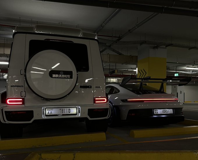 Two luxury vehicles—a white Brabus 800 SUV (license plate 78110) and a silver Porsche 911 GT3 (license plate 40451)—are parked side by side in an underground garage, symbolizing the crypto trader's sacrifice of high-end possessions during the bear market in pursuit of Bitcoin gains. The image visually represents the post's narrative of trading supercars for digital assets, with the dream of reclaiming such vehicles once Bitcoin nears $200,000.