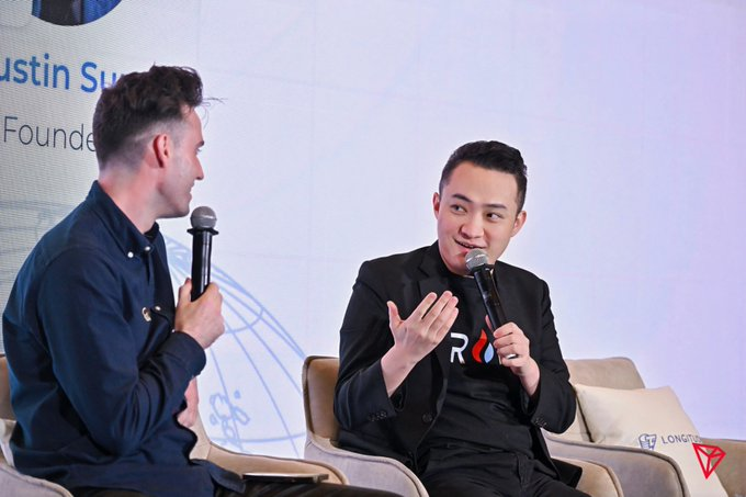 Justin Sun, Founder of TRON (visible on the backdrop), speaks into a microphone during a panel discussion, reflecting the company's active engagement in educational and industry events. His presence aligns with TRON's broader mission to promote blockchain literacy through workshops, university partnerships, and developer resources.