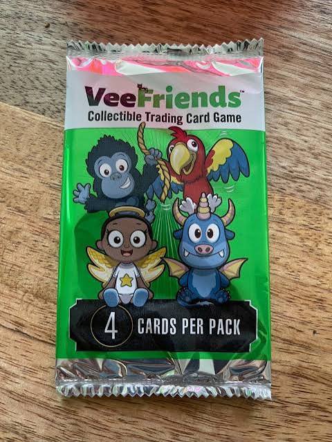 A sealed VeeFriends Collectible Trading Card Game booster pack featuring cartoon characters including a gorilla, parrot, angel, and dragon, advertising 4 cards per pack.