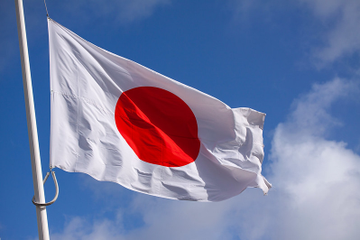 The image shows the Japanese flag—a white banner with a red circle—waving against a partly cloudy blue sky, symbolizing Japan as the "4th largest global economy" referenced in the post about the country preparing to launch Bitcoin and crypto ETFs.