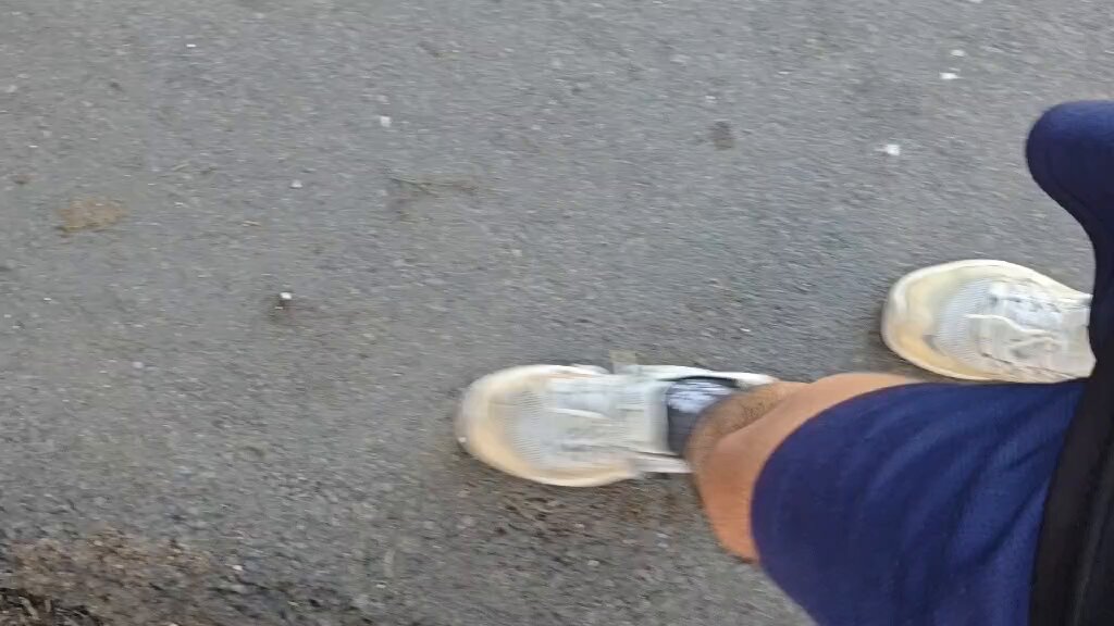 The image shows a person wearing blue shorts, white sneakers, and black socks walking down a street or sidewalk. They are looking at the camera while moving along their path. The photo appears to be taken from an angle that captures both the lower half of the person's body as well as the upper portion of their feet.

The post in question reads: "gm walking around with my @okx". This phrase is likely a reference to the person's social media account, where they might have tagged or captioned the photo. The image seems to be a casual snapshot of someone enjoying a walk outdoors while wearing comfortable athletic attire and sneakers.