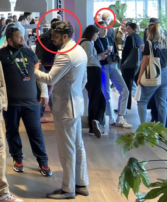 A casual networking event photo shows attendees mingling, with red circles highlighting two figures—one in the foreground being addressed by someone in a light blazer, and another in the background. The caption's realization matches the surprise of not noticing the second circled person (purportedly Brad Garlinghouse) was present in the same crowded room, emphasizing how easy it is to miss notable figures at busy gatherings.