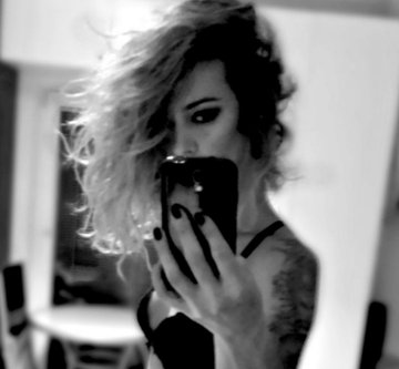 A black and white photo shows a person with tousled hair taking a mirror selfie with a phone, their face partially obscured. The moody, artistic aesthetic aligns with the "Artist & Art" theme of the post.