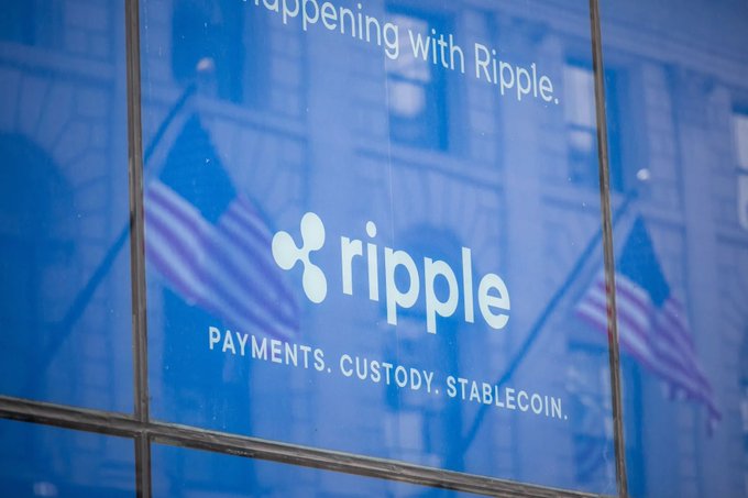 A blue-tinted photograph of the Ripple logo on a window, reading 'PAYMENTS. CUSTODY. STABLECOIN.' with American flags visible in the reflection.