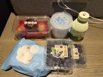 The image shows a variety of food items, including fruits such as blueberries and apples, snacks like chips, and drinks like milk and juice. The scene appears to be set up for a meal or snack time, with these items arranged on a table. The post is titled " Crypto Survival Plan Day19 晚间水果&内裤&一次性内裤外卖-6.59U ｜今天依旧使用Bitget Wallet U卡进行消费 出来晃悠", which suggests that the person who set up this scene is likely preparing for a camping trip or an outdoor adventure where they need to bring their own food and drinks. The presence of these items indicates that they are planning to have a variety of options available during their time outdoors, ensuring they stay well-fed and hydrated throughout their journey.